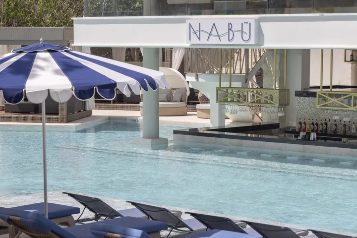 The NABÚ swim-up bar beside the resort pool, with blue loungers and striped umbrellas.