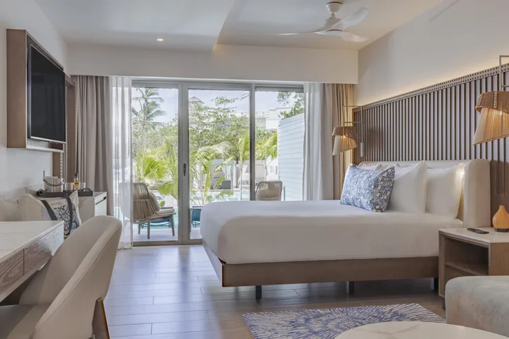 King bed and desk in a Luxury Junior Suite Swim Out with Butler, with sliding doors opening toward the pool terrace.