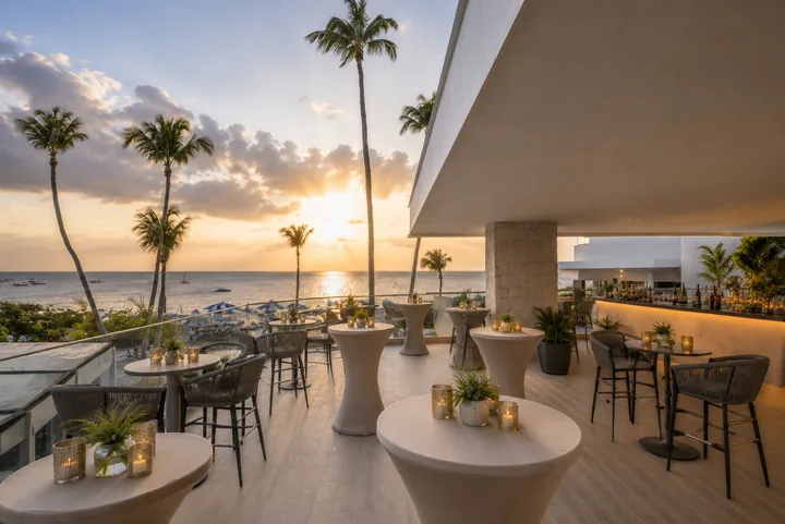 Open-air tables and bar seating at The Studio, with palms and a sunset over the sea.